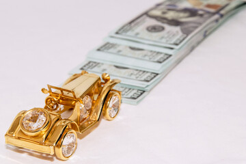 Miniature golden car close up. In the background is a stack of 100 dollar bills.