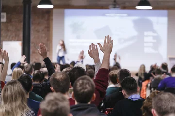 Erwachsene Studenten in einem großen Konferenzsaal hören einer Sprecherin zu und heben die Hände, um die Frage der Sprecherin zu beantworten. Geschäfts- und Unternehmerkonzept. Publikum im großen Klassenzimmer. © Feel good studio