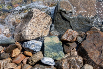 Rocks and pebbles on the shore in the water, various colors and textures