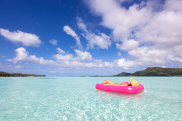 Woman relaxes on pink inflatable on clear turquoise water under the sun during tropical island vacation in Bora Bora