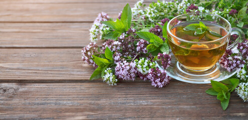 Freshly made herbal tea in a glass cup with mint and fresh oregano flowers on a wooden table with copy space. Herbal treatment.
