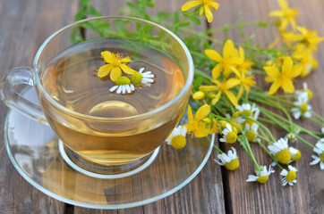 Freshly made St John's wort tea with chamomile in a glass cup and fresh flowers on a wooden table...