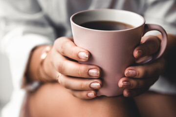 Woman in a white t-shirt holds morning coffee in a pink ceramic cup. Manicure. Front view