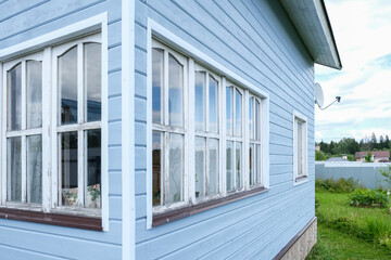 Fototapeta premium White windows of a small tiny frame house with blue walls,a country residence in sunny summer day