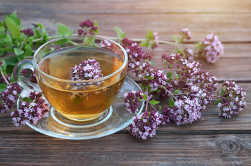 Aromatic herbal tea in a glass cup and fresh oregano flowers on a old wooden table. Healthy tea concept.