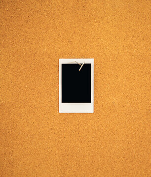 A Blank mini vertical Instant picture pinned to a corkboard  with a t-pin pushpin.