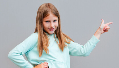 Cute cheerful blonde young female smiling broadly at camera and pointing fingers away, showing...