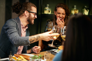 Group of friends in a restaurant, having diner and toasting with white wine.