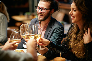 Group of friends in a restaurant, having diner and toasting with white wine.