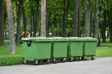 Four green trash cans on the wheels in the park. Recycled garbage, bins, waste. Ecological mission,...