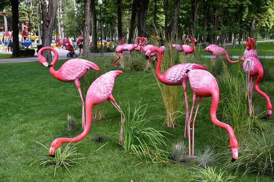 Artificial pink flamingos statues on the grass. Funny view for the visitors in the park, enjoyable time, summer relaxing. 