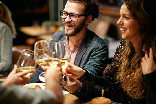 Group Of Friends In A Restaurant, Having Diner And Toasting With White Wine.