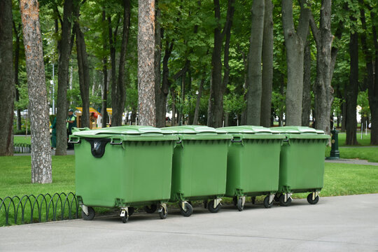 Four green trash cans on the wheels in the park. Recycled garbage, bins, waste. Ecological mission, save the planet from danger pollution