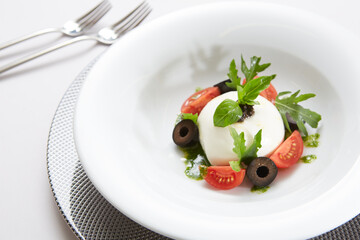 Traditional authentic soft and creamy fresh Italian burrata cheese shaped as white round ball over Italian tomatoes topped with rucola along side pesto reduction