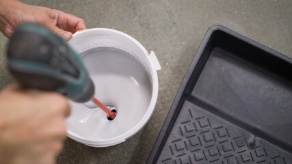 The white paint is mixed in a bucket with a drill. Drill paddle mixer on a bucket with white paint,...