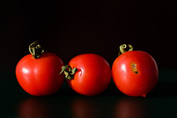 Three ripe tomatoes lie next to each other in front of a dark background, two of which are intact...