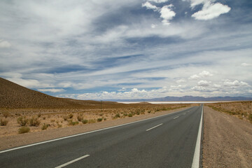 Naklejka premium Traveling along the empty desert road. Asphalt highway across the arid valley and mountains under a beautiful sky. 