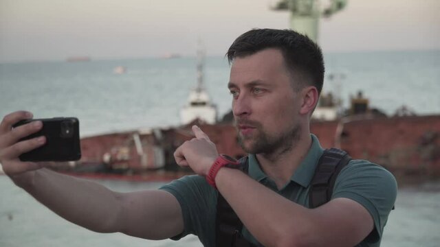 Man blogger records video blog on mobile phone for social media about accident of wreck tanker Delfi with oil in Odessa. Journalist reports on pollution of sea with oil products. Ecology problems