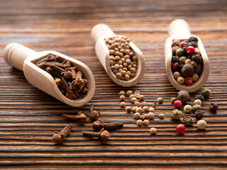 Various spices on a wooden background. Cloves, coriander seeds and peppers in wooden spoons. Selected sharpness. Macro