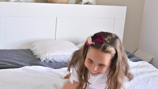 The child is having fun on the bed, jumping and laughing. Little girl in pajamas and shabby bedroom. Morning time at home. High quality 4k footage