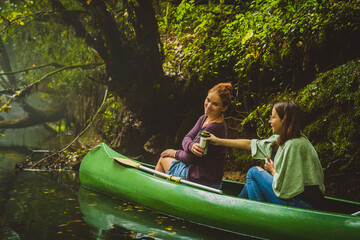 Drinking beer in a canoe, two young women passing a beer can to each other on a misty cold and...