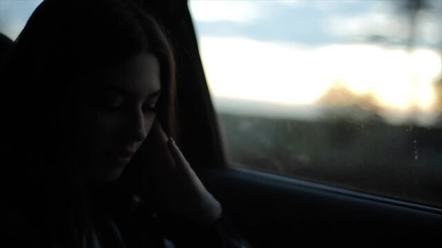 A romantic young girl looks out the car window on the evening landscape. Close-up. Blurred background. Slow motion