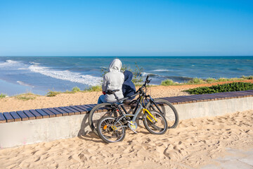 Fototapeta premium Back view of family looking at the beach, tourists use bicycles. Sunny blue sky outdoors background. Ecotourism activity concept.