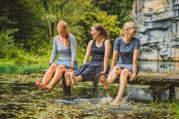 Three young women  relaxing on a wooden pier and splashing their feet into cold water. Picturesque...