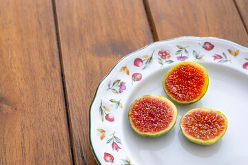 Three figs cut in half on a decorated plate on a teak table, selective focus