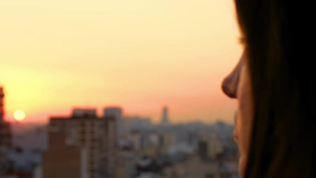 Woman looks out at urban city in the distance as day turns to night Golden Hour Sunset View With Clouds 180fps