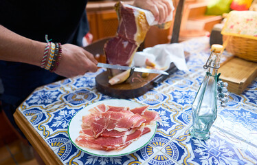 Person cutting ham from the leg of the pork ham with a long knife. Spanish typical food
