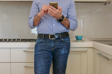 man drinks a coffee in the kitchen and in the meantime looks at the smartphone