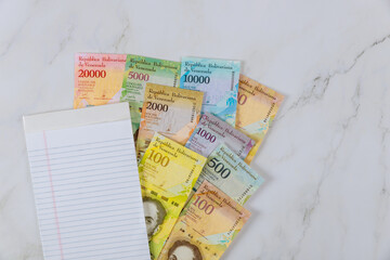 Office table with a banknote with different paper bills currency Venezuelan Bolivar a blank notepad