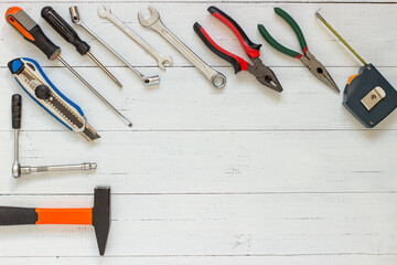 Different repair and construction tools on wood texture background. Wrenches, screwdrivers, stationery knife, tape measure, hammer and pliers on white background with copy space.