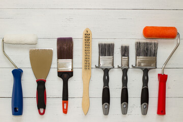 Spatula for application of putty, brushes and rollers for painting, and cord brush on a white wooden background . Top view.