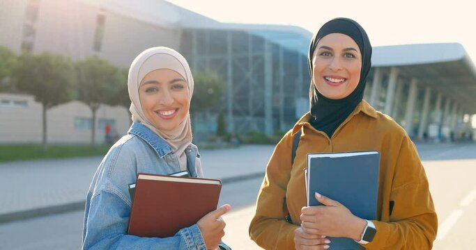 Portrait young Arabic beautiful women in headscarves smiling and holding textbooks books. Pretty Arabian females students in hijabs at street. Islamic happy girls. Education for muslims. Educational.