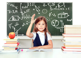 Happy and cute teen schoolgirl raising hand in classroom