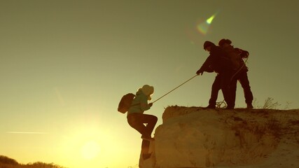 climbers climb mountain on a rope. male tourist helps a girl traveler to climb mountain. Travel and adventure in mountains at sunset. teamwork of tourists in sun. freedom and adventure concept