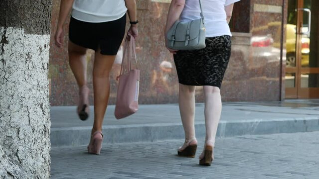 Two women in dark skirts and white blouses walk towards the office door. A pretty young woman in mini skirt with a beautiful figure gracefully walks in high platform shoes and heels. Ladies go to work