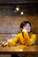 One young Asian guy in yellow clothes is drinking beer in an empty cafe and looking in window, waiting his friends. Copy space