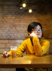 One young Asian guy in yellow clothes is drinking beer in an empty cafe and looking in window, waiting his friends. Copy space