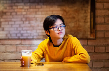One young Asian guy in yellow clothes is drinking beer in an empty cafe and looking in window, waiting his friends. Copy space