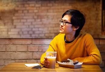 One young Asian guy in yellow clothes is drinking beer in an empty cafe, waiting his friends. Scrolls the news feed. Copy space