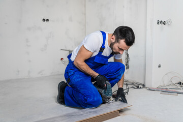 Carpenter in blue work clothes sawing laminate boards with an electric saw