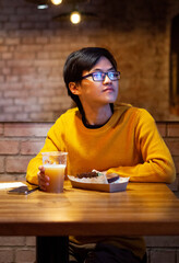 One young Asian guy in yellow clothes is drinking beer in an empty cafe, waiting his friends. Scrolls the news feed. Copy space