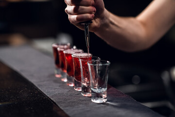 bartender pours red alcohol into shots on the bar, bartender's show.