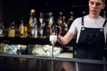 a young bartender pours champagne into a glass from a bottle on the bar.
