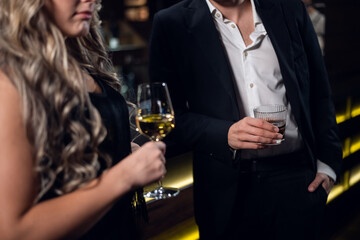 a blonde girl in a black dress holding a glass of champagne, a man in a jacket holding a glass of whiskey, close-up.
