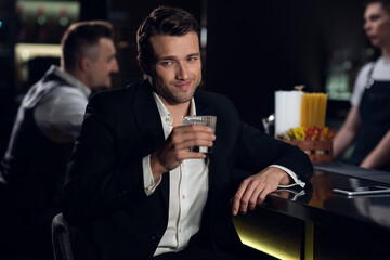 portrait of a young man in a shirt and jacket at the bar with a cocktail in his hands.