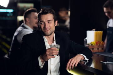 a beautiful man poses for a photo at the bar of a restaurant with a cocktail in his hands, portrait.